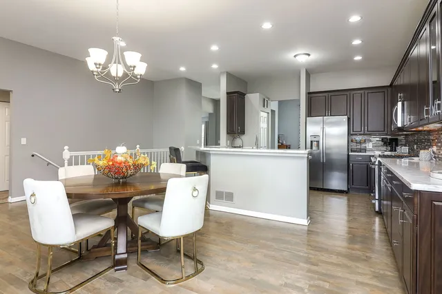 a kitchen with stainless steel appliances kitchen island granite countertop a refrigerator a stove a microwave oven a dining table and chairs with wooden floor