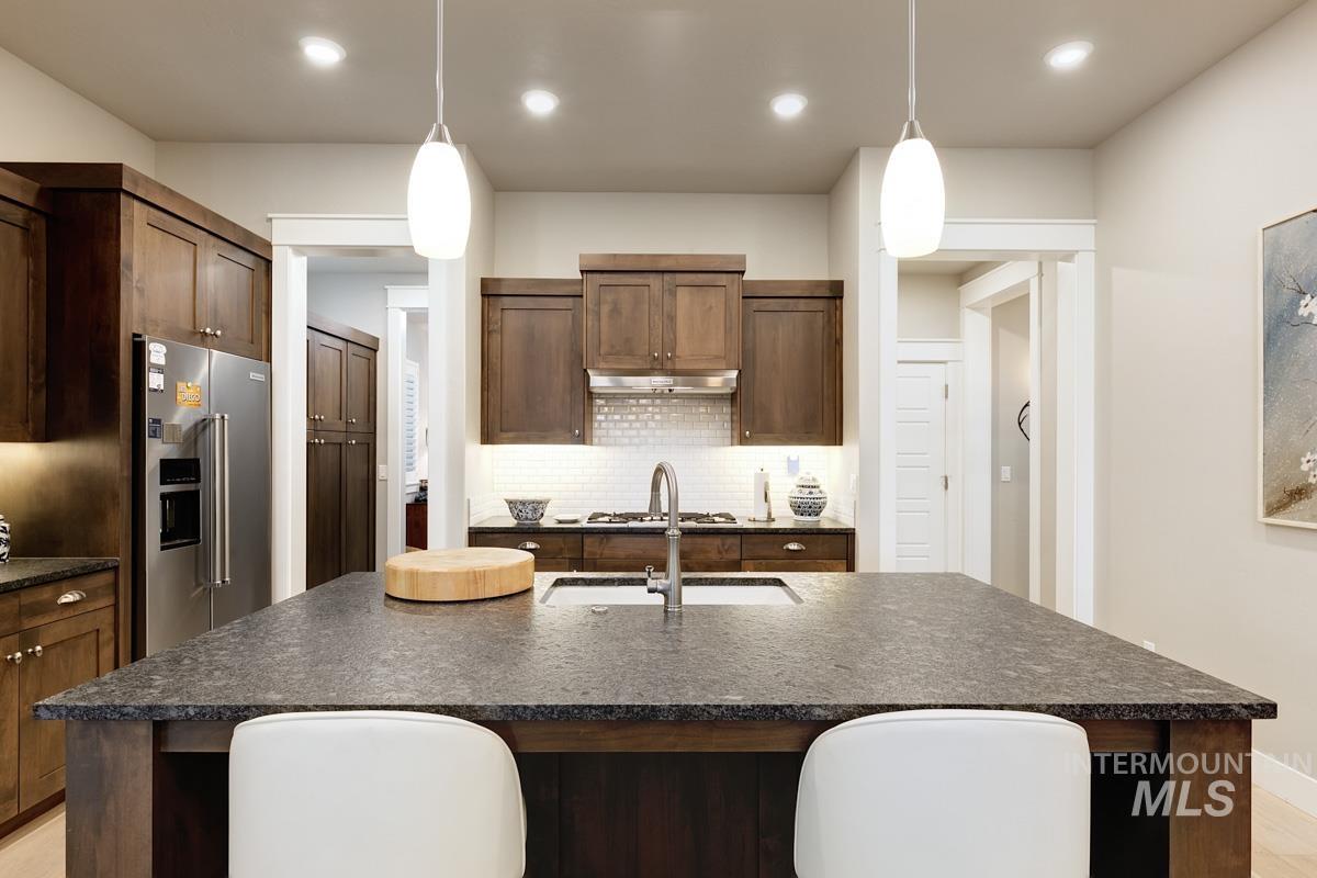 410 West Lockhart Lane Meridian, ID 83646 - Photo 15 of 41 Kitchen featuring a center island with sink, hanging light fixtures, stainless steel appliances, tasteful backsplash, and dark stone counters