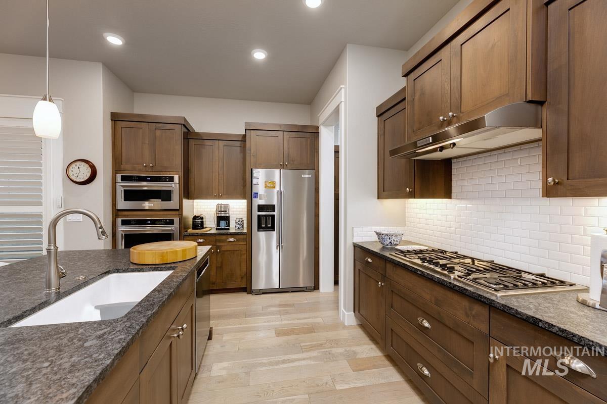 410 West Lockhart Lane Meridian, ID 83646 - Photo 16 of 41 Kitchen featuring stainless steel appliances, light wood finished floors, dark stone counters, and decorative light fixtures