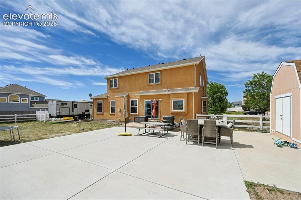 8347 Tibbs Road Peyton, CO 80831 - Photo 35 of 39 Expansive concrete patio with stucco exterior, rear double doors, multiple windows, and a detached storage shed