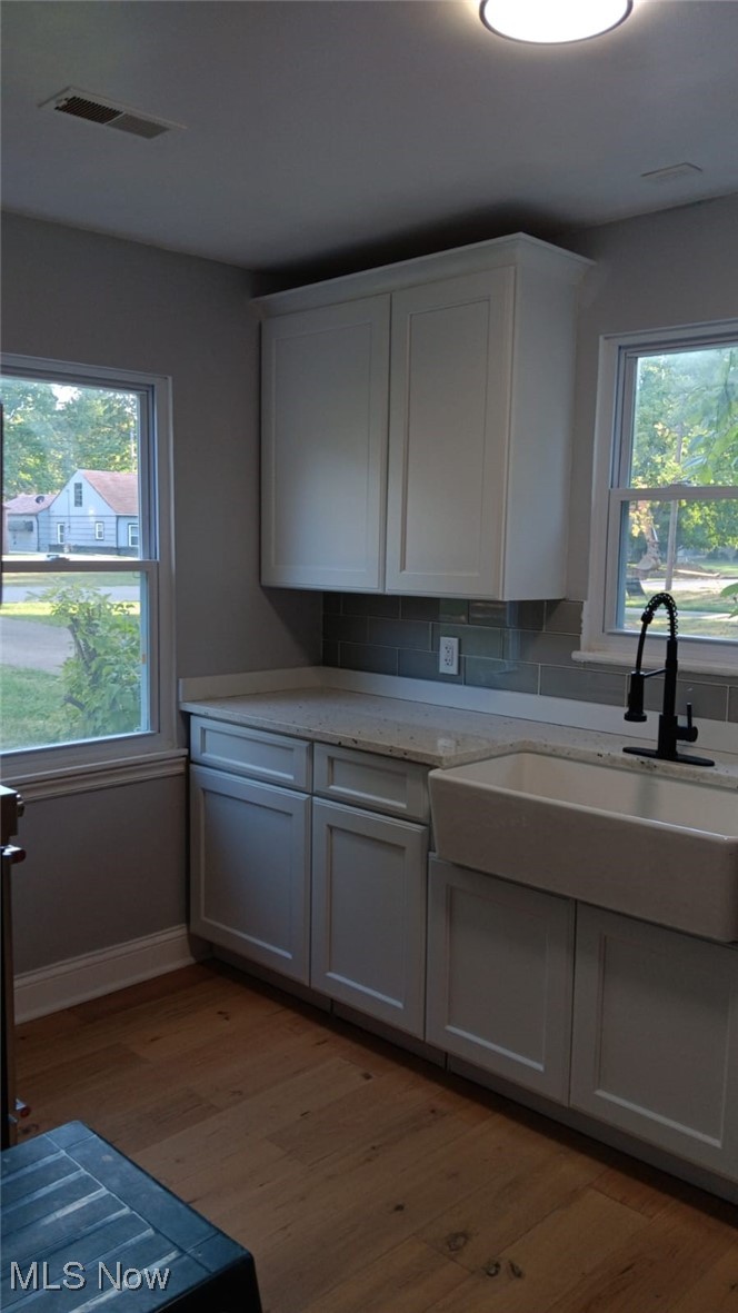 3999 Lancaster Road South Euclid, OH 44121 - Photo 11 of 17 Kitchen with light stone countertops, decorative backsplash, white cabinets, sink, and light hardwood / wood-style floors