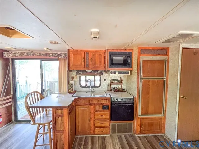 a kitchen with stainless steel appliances granite countertop a stove a refrigerator a sink a dining table and chairs with wooden floor