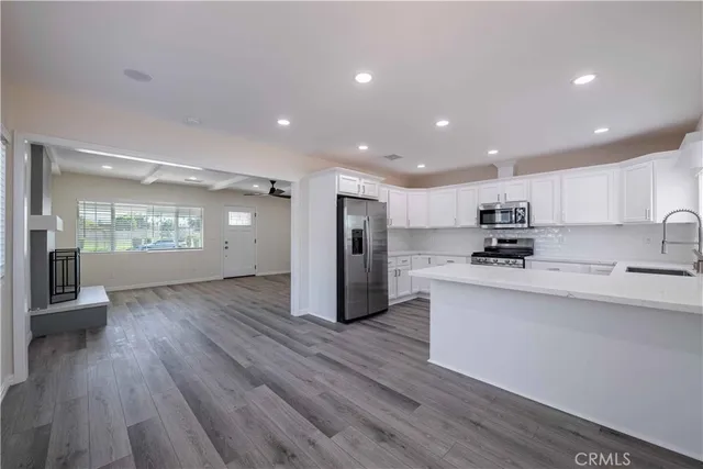 a open kitchen with stainless steel appliances granite countertop a refrigerator a sink dishwasher a stove and white countertops with wooden floor