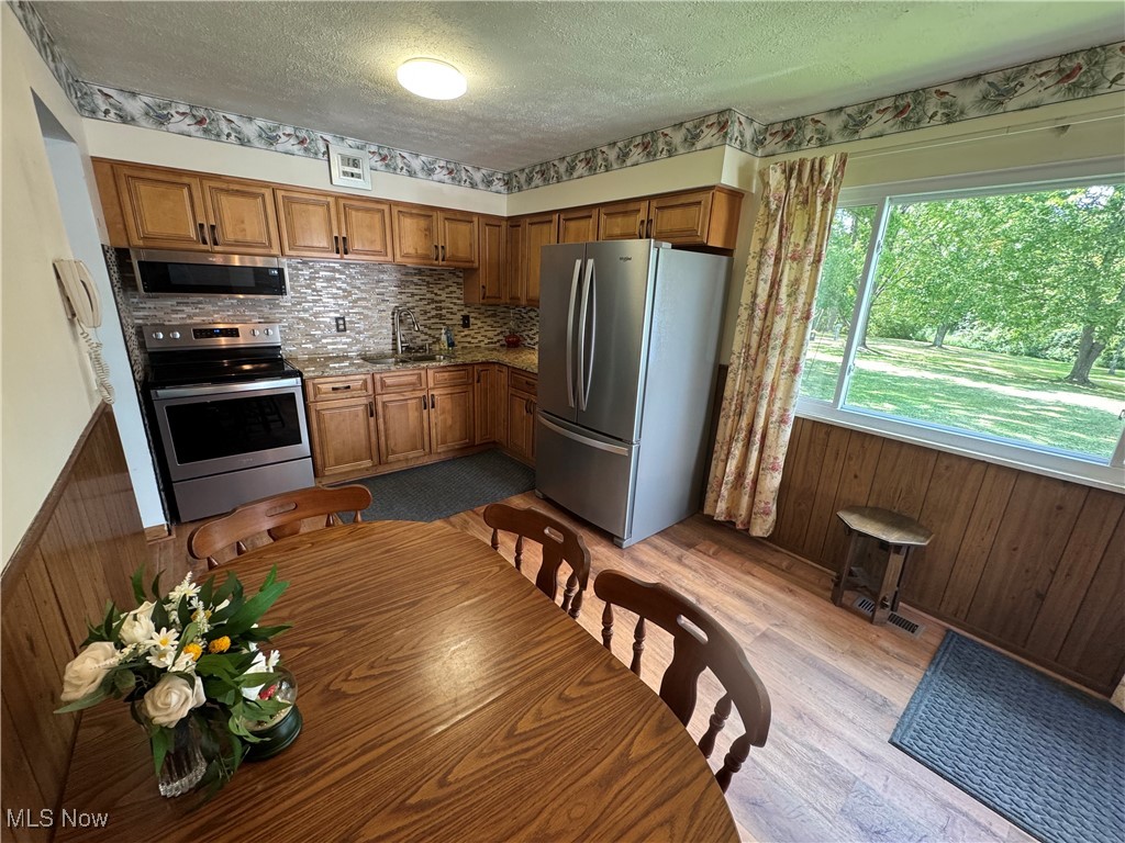 8810 Auburn Road Chardon, OH 44024 - Photo 9 of 22 Kitchen featuring appliances with stainless steel finishes, brown cabinetry, light wood finished floors, backsplash, and a textured ceiling