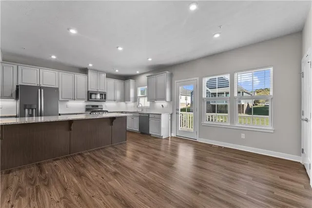 a kitchen with stainless steel appliances granite countertop a refrigerator a sink dishwasher a stove and a microwave oven on the wooden floor