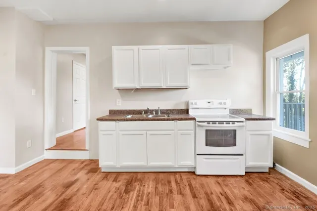 a white kitchen with granite countertop a stove top oven a sink and white cabinets with wooden floor