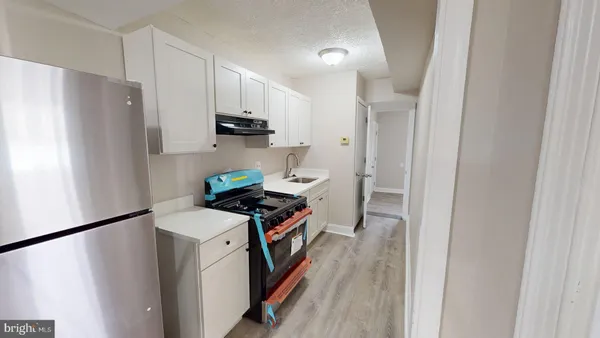 a kitchen with stainless steel appliances a refrigerator a sink a stove and white cabinets with wooden floor