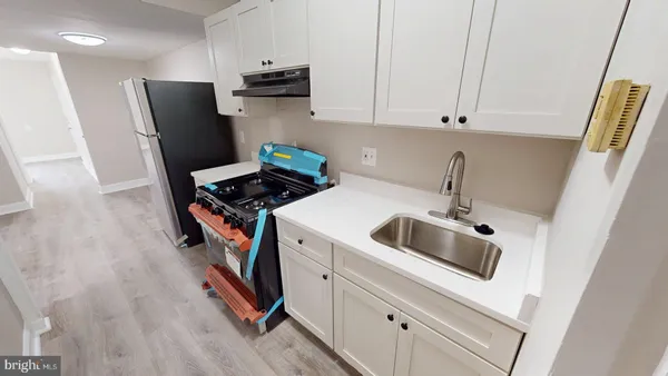 a kitchen with stainless steel appliances a refrigerator a sink a stove and white cabinets with wooden floor