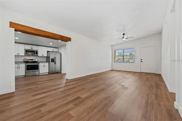 an empty room with wooden floor kitchen view and a window