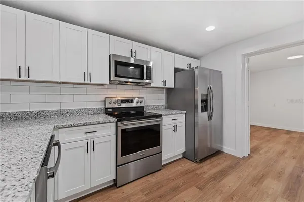 a kitchen with stainless steel appliances white cabinets a sink a stove a refrigerator and microwave