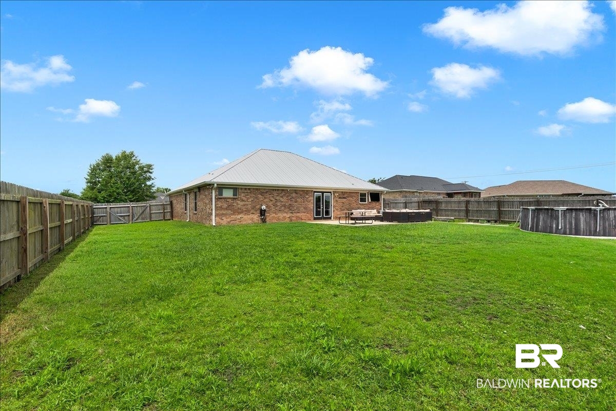 8952 Sherman Road Foley, AL 36535 - Photo 38 of 41 Spacious backyard featuring a manicured lawn, full privacy fencing, and a brick exterior with a metal roof