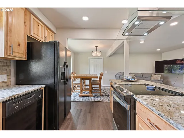 a kitchen with stainless steel appliances granite countertop a refrigerator a sink dishwasher a stove and a dining table with wooden floor