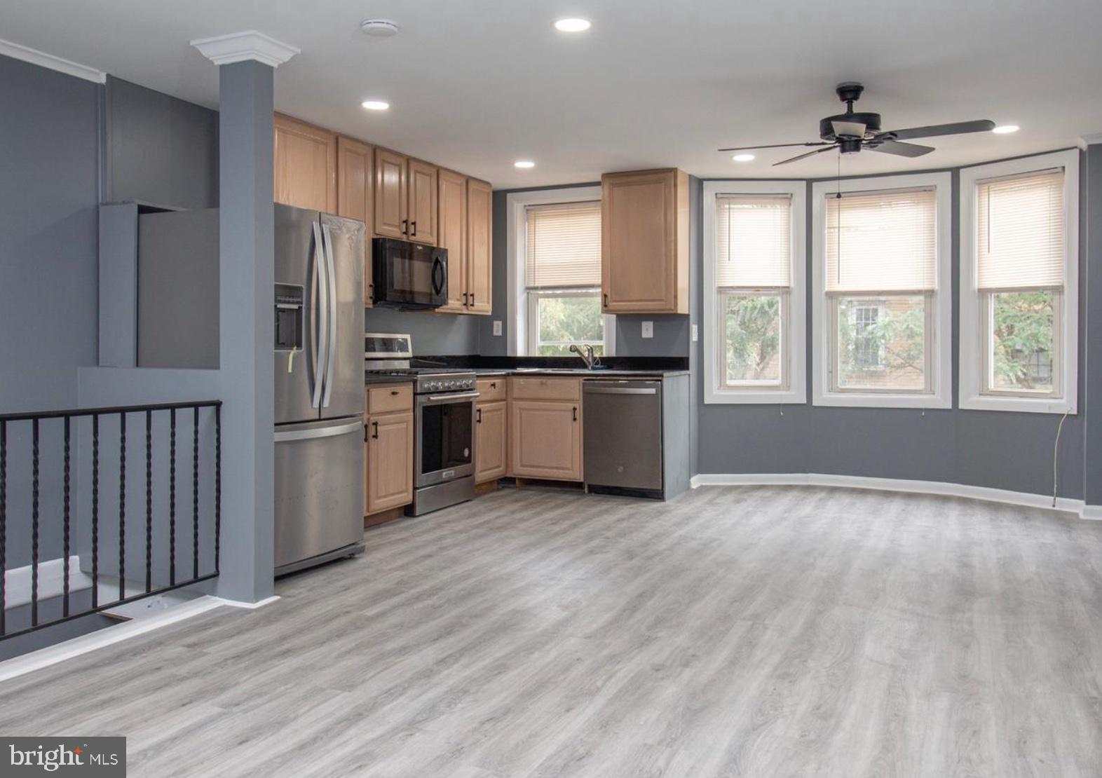 a kitchen with stainless steel appliances granite countertop a stove top oven a sink dishwasher a refrigerator and a microwave oven on the wooden floor