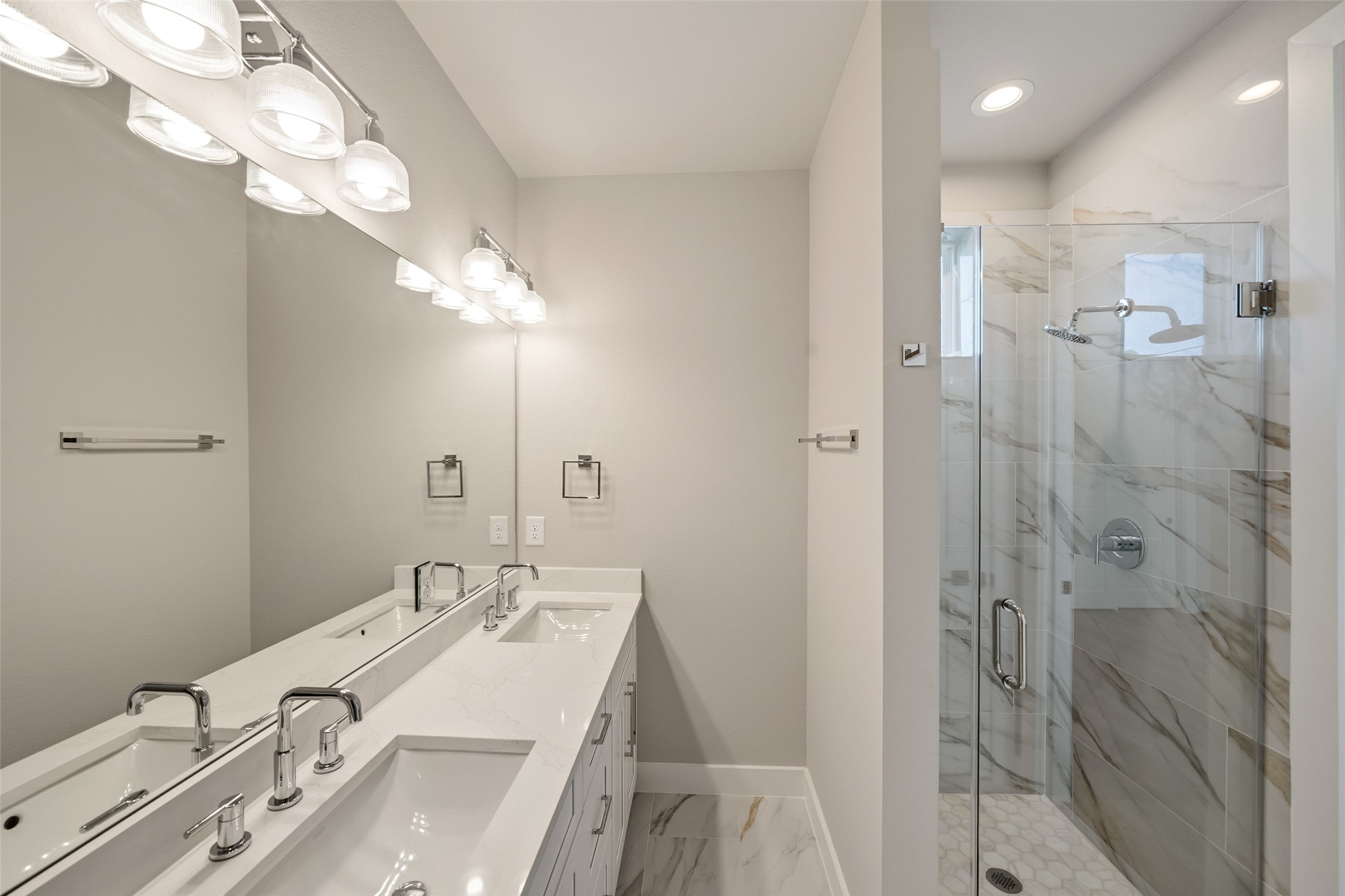 3422 Elser Street Houston, TX 77009 - Photo 13 of 26 This modern bathroom features a double vanity with sleek faucets, ample lighting, and a spacious glass-enclosed shower with elegant marble-style tiles.