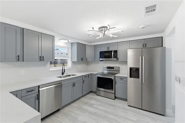 a kitchen with stainless steel appliances granite countertop a sink a stove a refrigerator with white cabinets and wooden floor