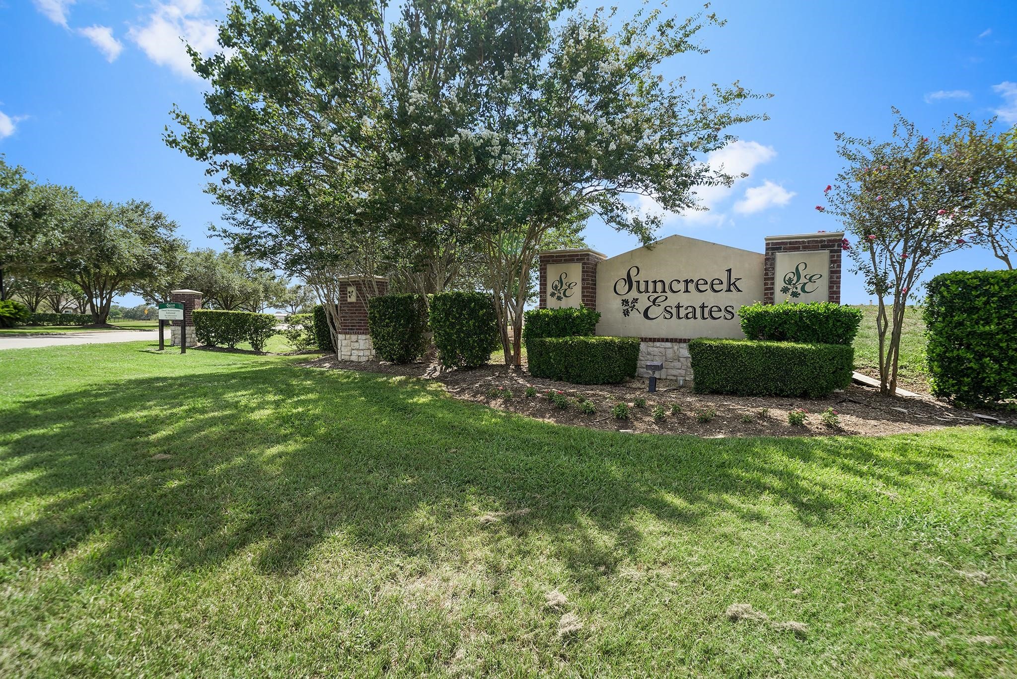 This photo shows the entrance to Suncreek Estates, featuring a well-maintained sign surrounded by lush greenery and trees, suggesting a welcoming and serene neighborhood atmosphere.