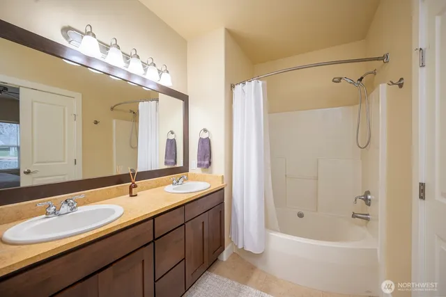 a bathroom with a double vanity sink a large mirror and a bathtub