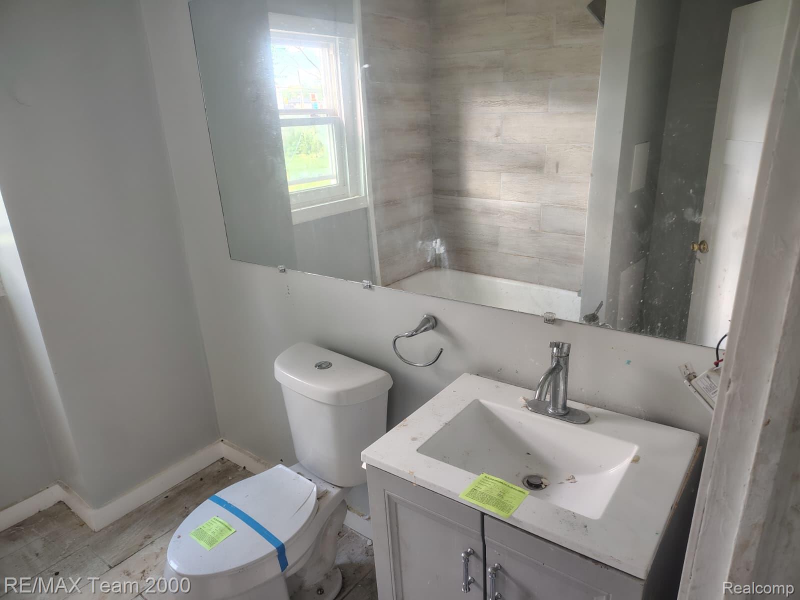 8860 Appoline Street Detroit, MI 48228 - Photo 25 of 45 Bathroom featuring a single window, a tub with tiled surround, a vanity with an undermount sink, and a toilet