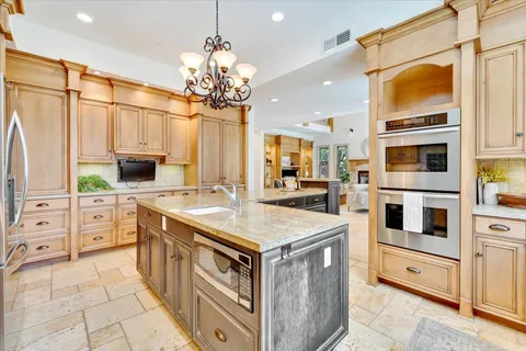 a kitchen with stainless steel appliances kitchen island granite countertop a stove top oven a sink dishwasher and white cabinets with wooden floor