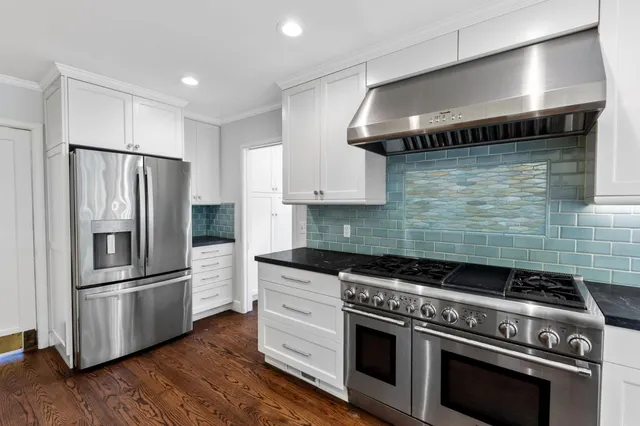 a kitchen with stainless steel appliances a sink a stove a refrigerator cabinets and a dining table with wooden floor