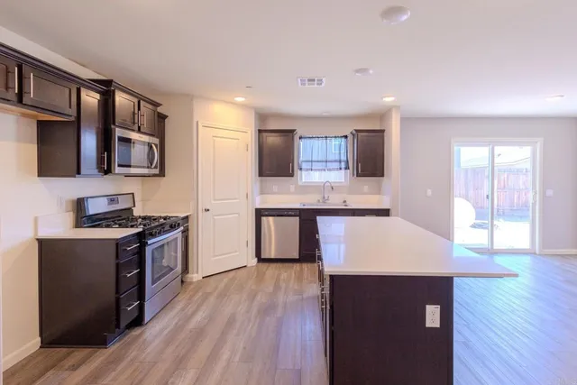 a kitchen with stainless steel appliances granite countertop a stove a sink dishwasher and a refrigerator with wooden floor