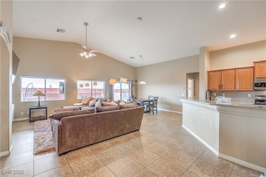 Living room featuring light tile patterned floors, high vaulted ceiling, visible vents, and a ceiling fan