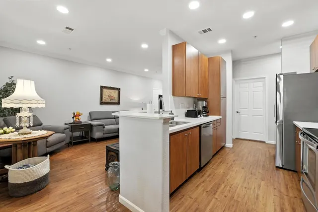 a kitchen with stainless steel appliances kitchen island granite countertop a stove a sink a refrigerator and white cabinets with wooden floor