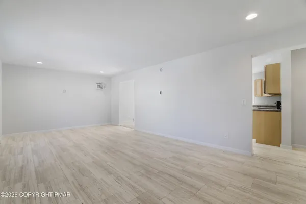 a view of an empty room with wooden floor and a kitchen