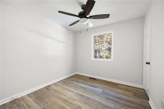 an empty room with wooden floor ceiling fan and windows