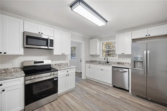 a kitchen with granite countertop a stove top oven a sink dishwasher a refrigerator and white cabinets with wooden floor