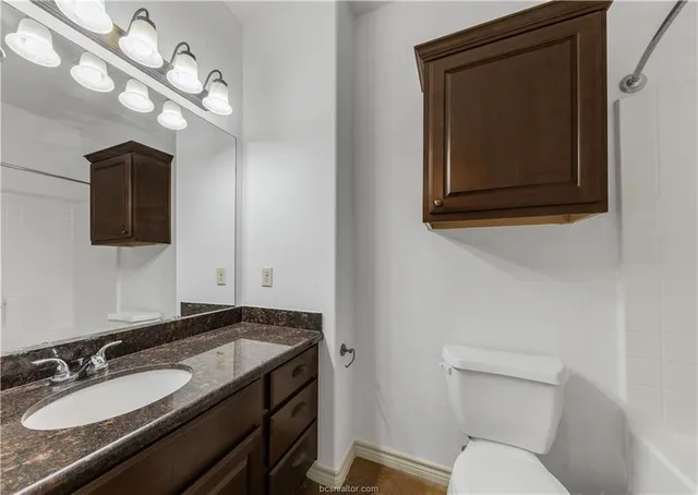 a bathroom with a granite countertop toilet sink and mirror