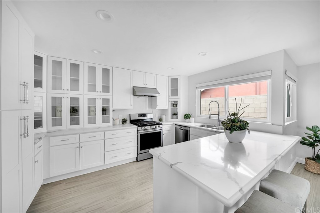 a large white kitchen with granite countertop a stove a sink a dining table and chairs