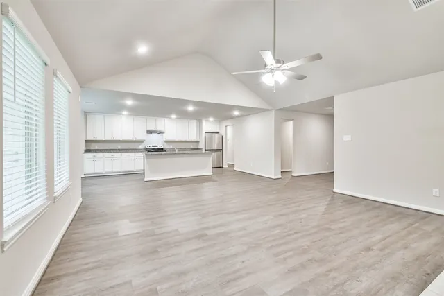 a view of an empty room and kitchen view with wooden floor