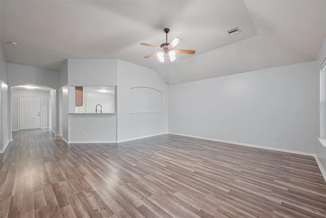 a view of an empty room with wooden floor and a ceiling fan