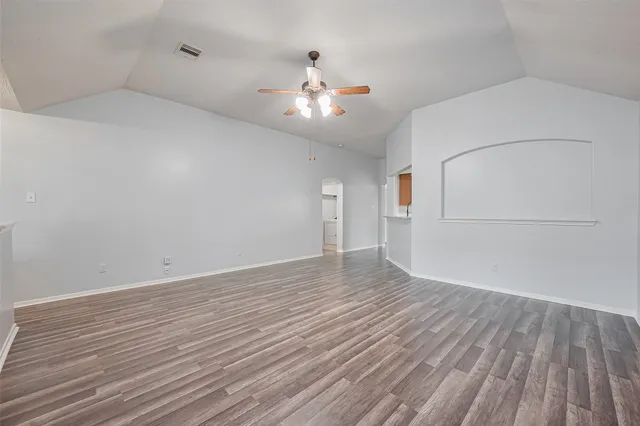 a view of an empty room with wooden floor and a ceiling fan