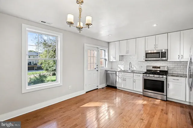 a kitchen with stainless steel appliances white cabinets a sink dishwasher a refrigerator and a stove with wooden floor