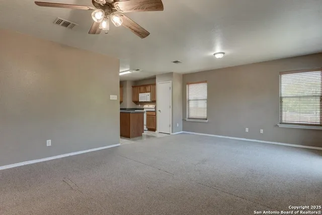 an empty room with chandelier fan and windows