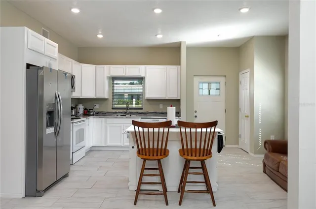 a kitchen with stainless steel appliances granite countertop a dining table chairs refrigerator and a sink