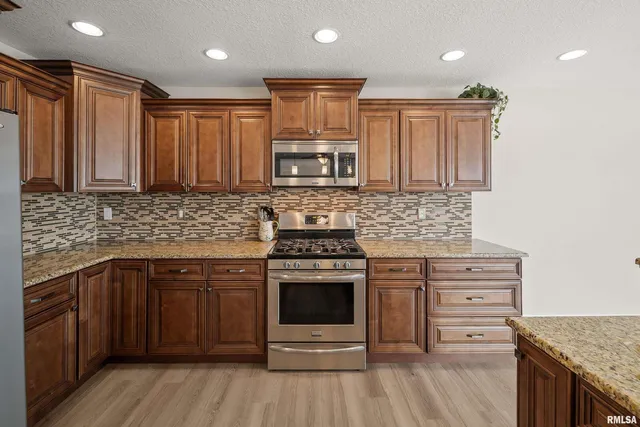 a kitchen with stainless steel appliances granite countertop a stove top oven a sink dishwasher a refrigerator and a microwave oven with wooden floor