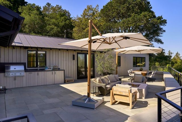 a view of a patio with a dining table and chairs under an umbrella with a barbeque
