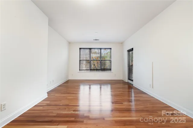 a view of an empty room with window and wooden floor