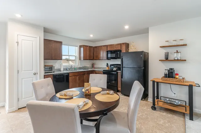 a kitchen with stainless steel appliances granite countertop a refrigerator a sink a stove a dining table and chairs