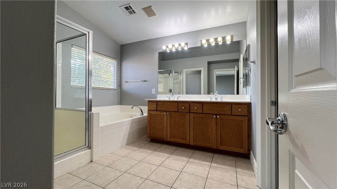 258 Rustic Club Way Las Vegas, NV 89148 - Photo 14 of 25 This primary bathroom features a double vanity, a soaking tub, and a separate glass-enclosed shower.