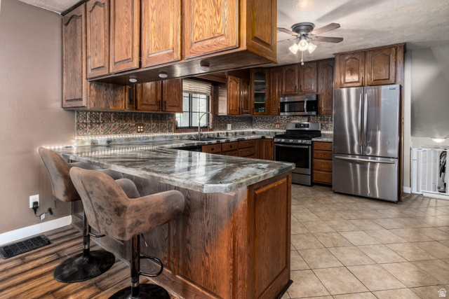 100 Third North Helper, UT 84526 - Photo 16 of 30 Kitchen featuring wood cabinetry, stainless steel appliances, a breakfast bar with stone-finish countertop, tile backsplash, and overhead ceiling fan