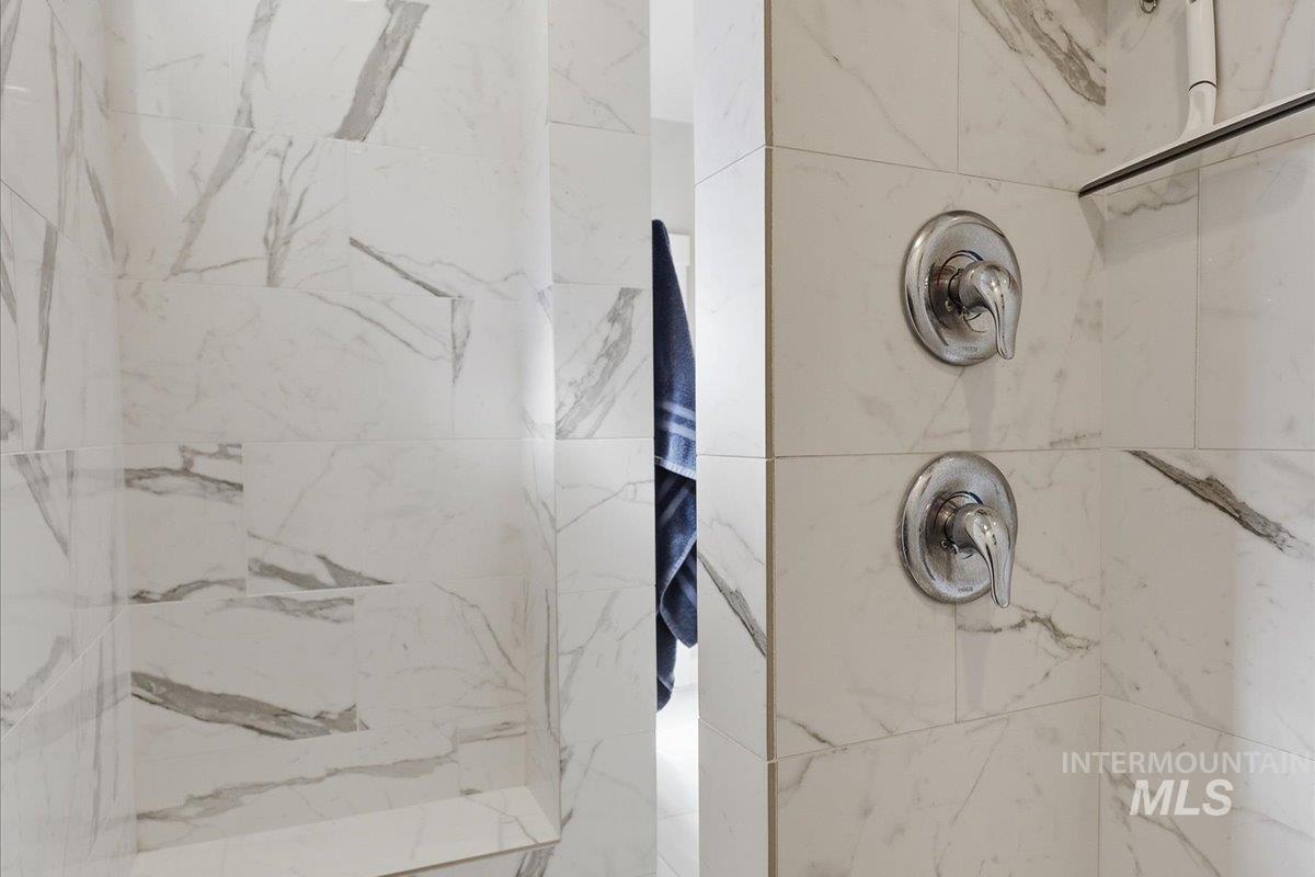 1303 West Brando Street Meridian, ID 83646 - Photo 28 of 49 Shower enclosure featuring large format white tile with gray veining, chrome fixtures, and a recessed niche