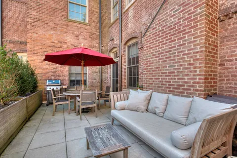 a view of a patio with a dining table and chairs under an umbrella with a barbeque grill and couches