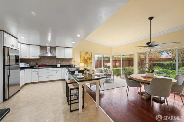 a living room with stainless steel appliances furniture a rug kitchen view and a large window