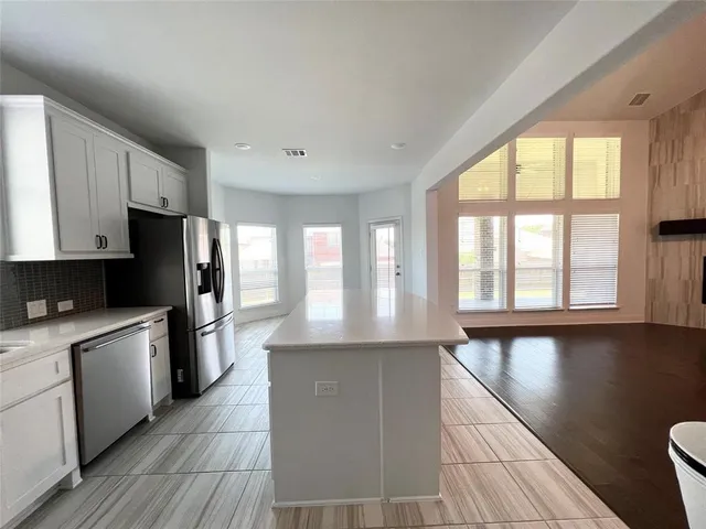 a large kitchen with granite countertop a stove a sink a refrigerator and white cabinets with wooden floor