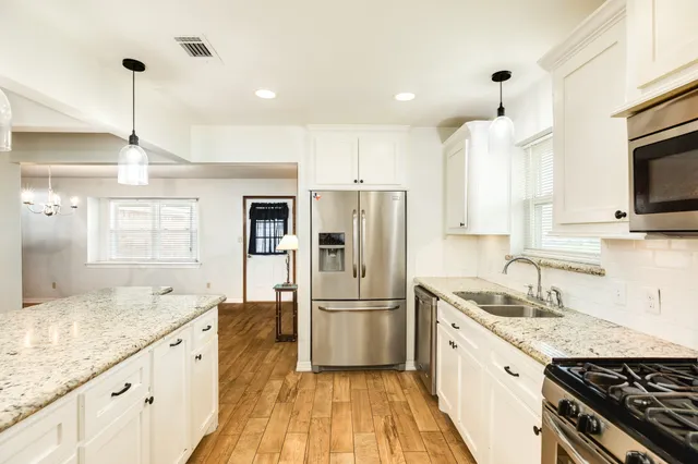 a kitchen with granite countertop a refrigerator a sink a stove and wooden floor