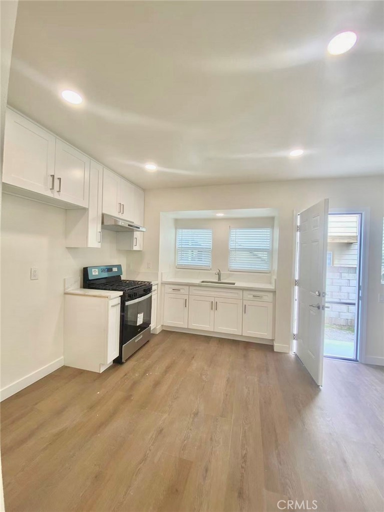 920 West Olive Avenue, Unit 1 Monrovia, CA 91016 - Photo 3 of 13 a large white kitchen with a refrigerator a stove top oven a sink and dishwasher with wooden floor